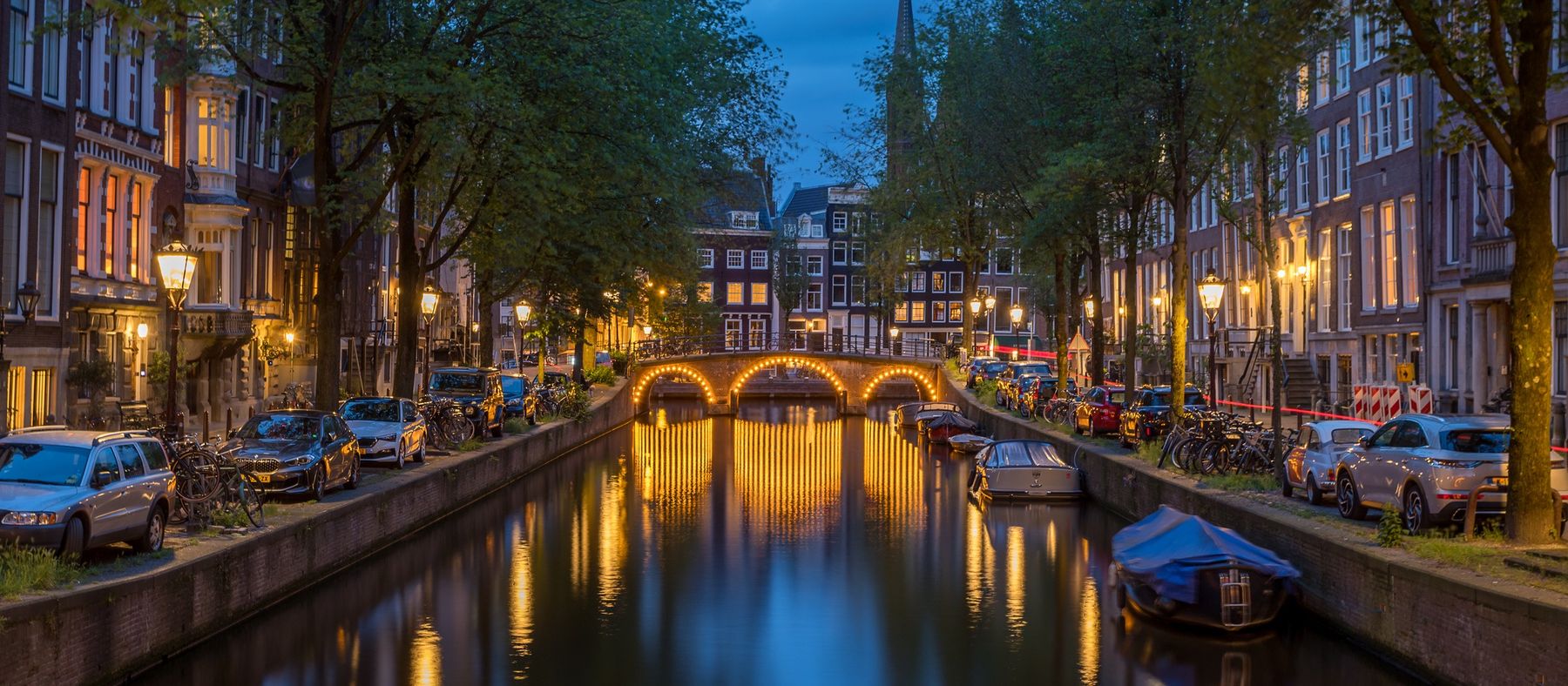 Amsterdam canal at dusk, with a lit bridge reflected in the water